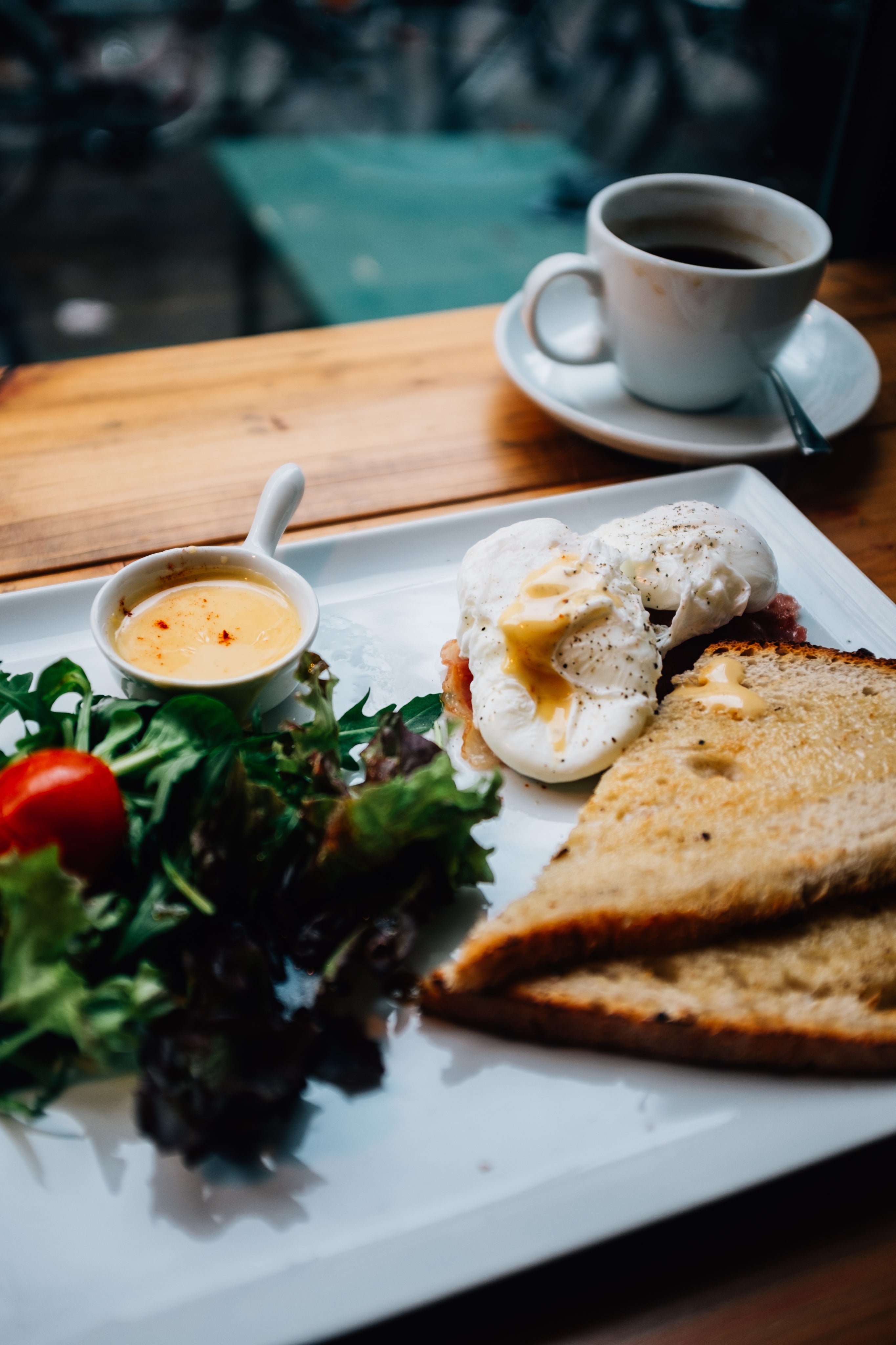 Assiette de brunch avec œufs pochés, toasts, salade fraîche et café servis sur une table en bois, Lumyeye permet de décrire entièrement cela grâce à votre voix.